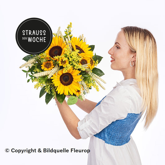 Strauß der Woche, gehalten von einer jungen Frau, mit Sonnenblumen, Getreideähren und weiteren kleinen Blumen in Gelbtönen. Dazu diverses Grün
