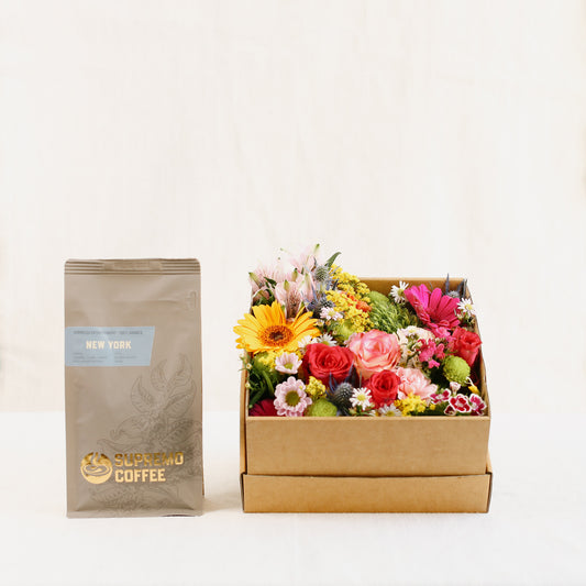 Eine Tüte feine Espresso-Spezialität „New York - Decaf“ (250 g als ganze Bohne) der Kaffeerösterei Supremo zusammen mit einer mit Blumen gefüllten Blumen-Box