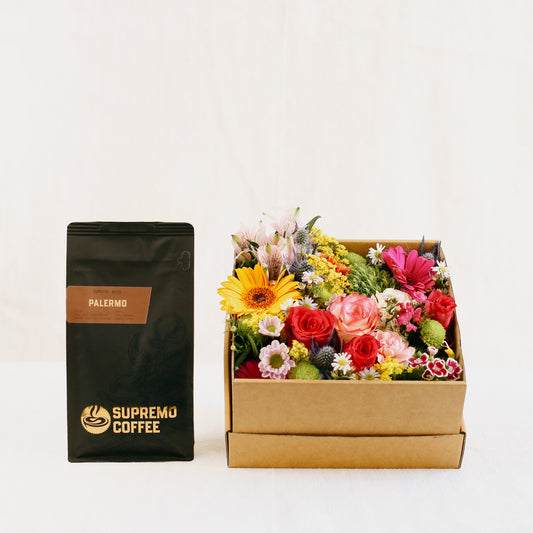 Eine Tüte feine Espresso-Spezialität „Palermo“ (250 g Espresso als ganze Bohne) der Kaffeerösterei Supremo. mit einer mit bunten Blumen gefüllten Blumen-Box