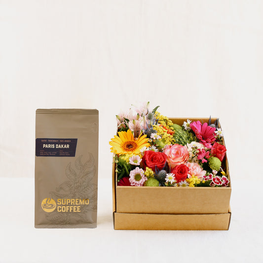 Eine Tüte feine Kaffeespezialität „Paris Dakar“ (250 g als ganze Bohne) der Kaffeerösterei Supremo. mit einer mit bunten Blumen gefüllten Blumen-Box