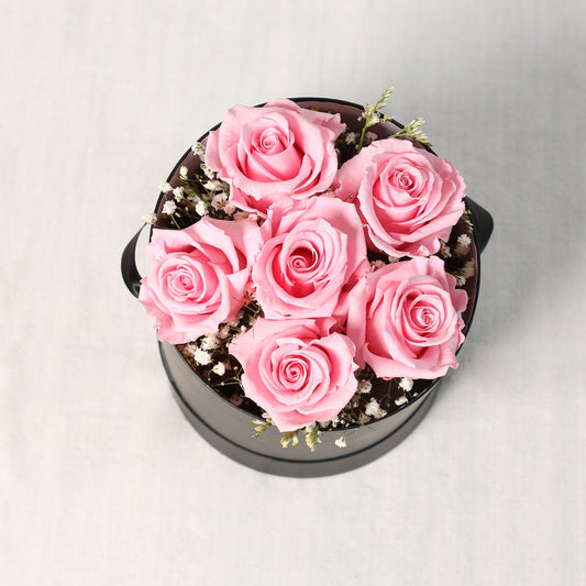 Draufsicht-eine edle, runde, schwarze Zylinder- Box mit rosa gefriergetrockneten Rosen und Schleierkraut