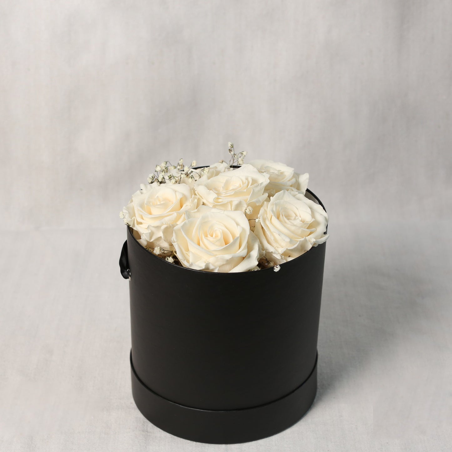 Vorderansicht-eine edle, runde, schwarze Zylinder- Box mit weißen, gefriergetrockneten Rosen und Schleierkraut