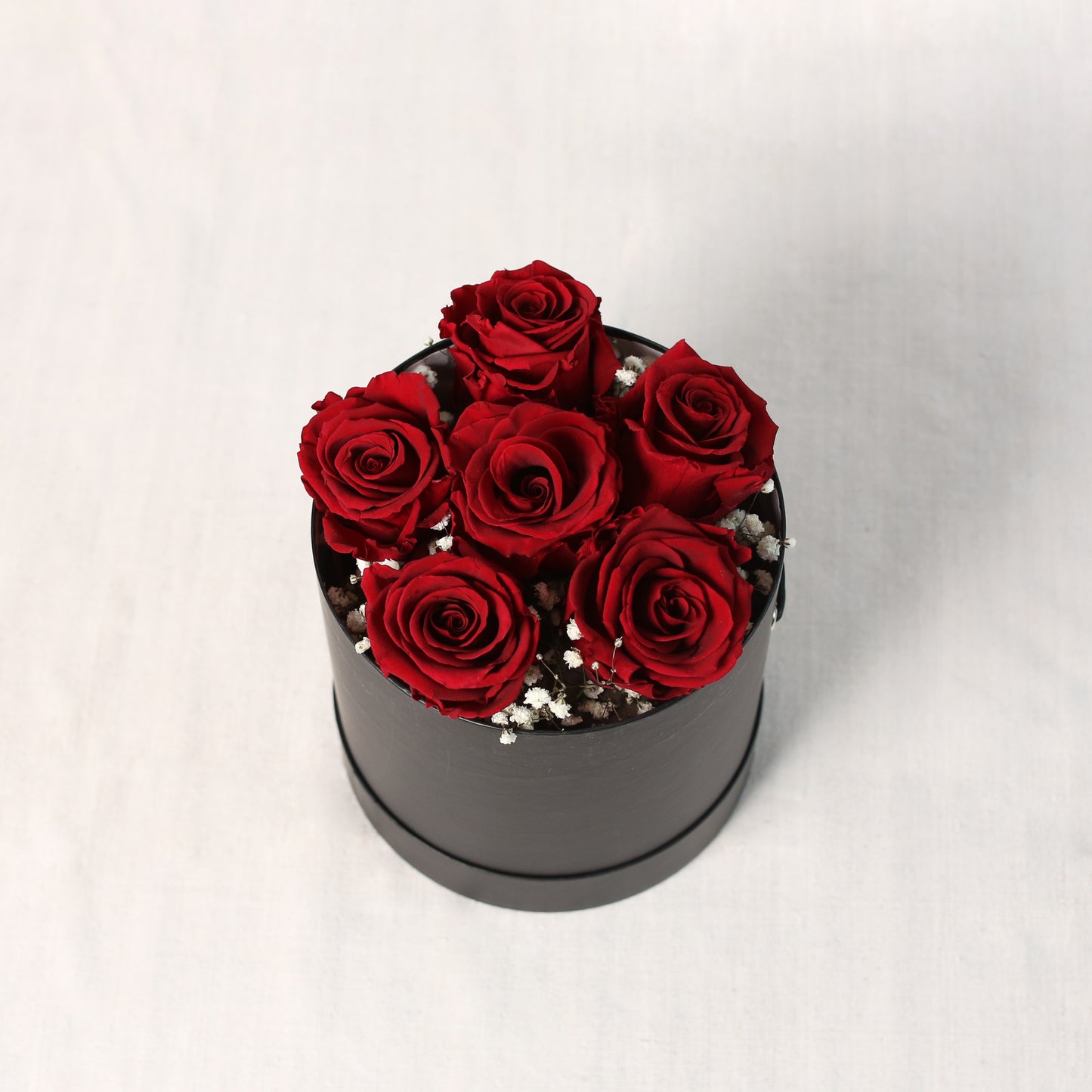 Schräge Draufsicht-eine edle, runde, schwarze Zylinder- Box mit roten, gefriergetrockneten Rosen und Schleierkraut